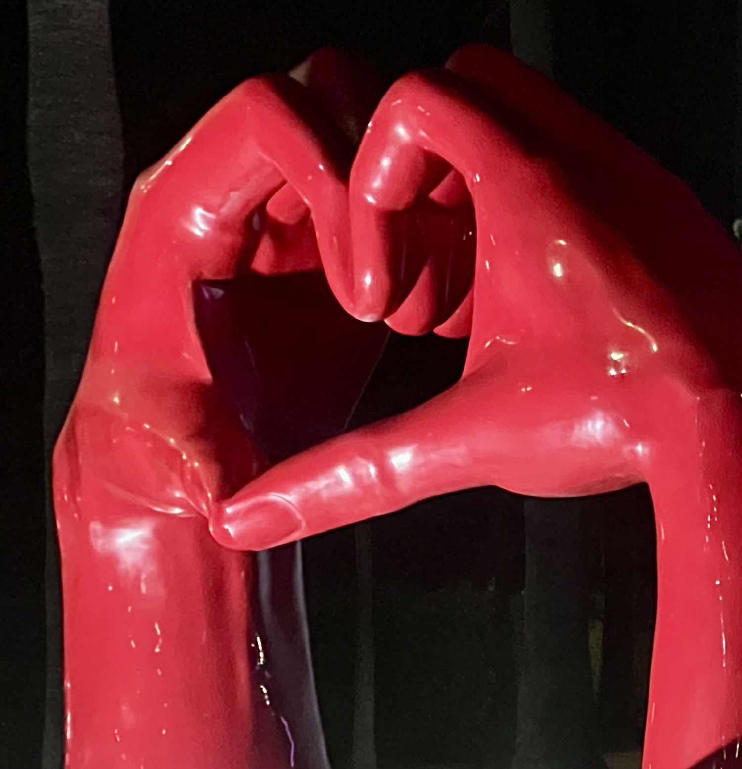 A red lacquered sculpture of two hands forming a heart against a dark background.