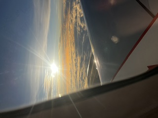 Golden clouds and sunbeams seen through an airplane window high above the earth.