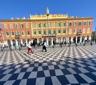 The checkered plaza of Place Masséna stretching toward pastel buildings under a bright sky.