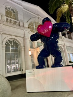 A glossy navy gorilla sculpture holding a pink heart outside a lit historic building at night.