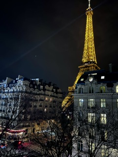 The Eiffel Tower lit gold at night above Parisian rooftops and glowing windows.