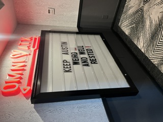 A hotel marquee board reading 'Keep Austin weird and well rested' beneath a red neon sign.