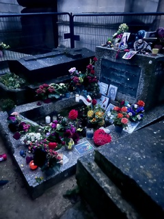 A grave in Père Lachaise blanketed with flowers, photographs, and handwritten notes.