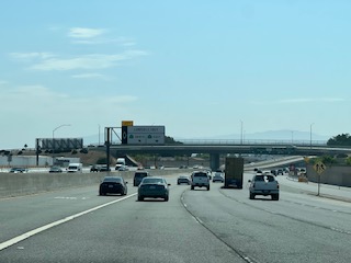 An open highway stretching toward distant hills under a pale summer sky.