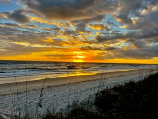 A golden sunset breaking through clouds over an empty stretch of shoreline.