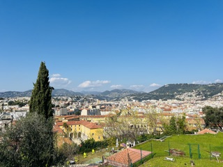 A view over the terracotta rooftops and green hills of Nice toward the Mediterranean.